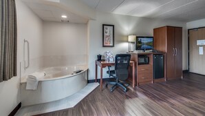 A hotel room with a bathtub, desk, chair, microwave, refrigerator, and a TV. - AmericInn by Wyndham Coon Rapids (Coon Rapids)