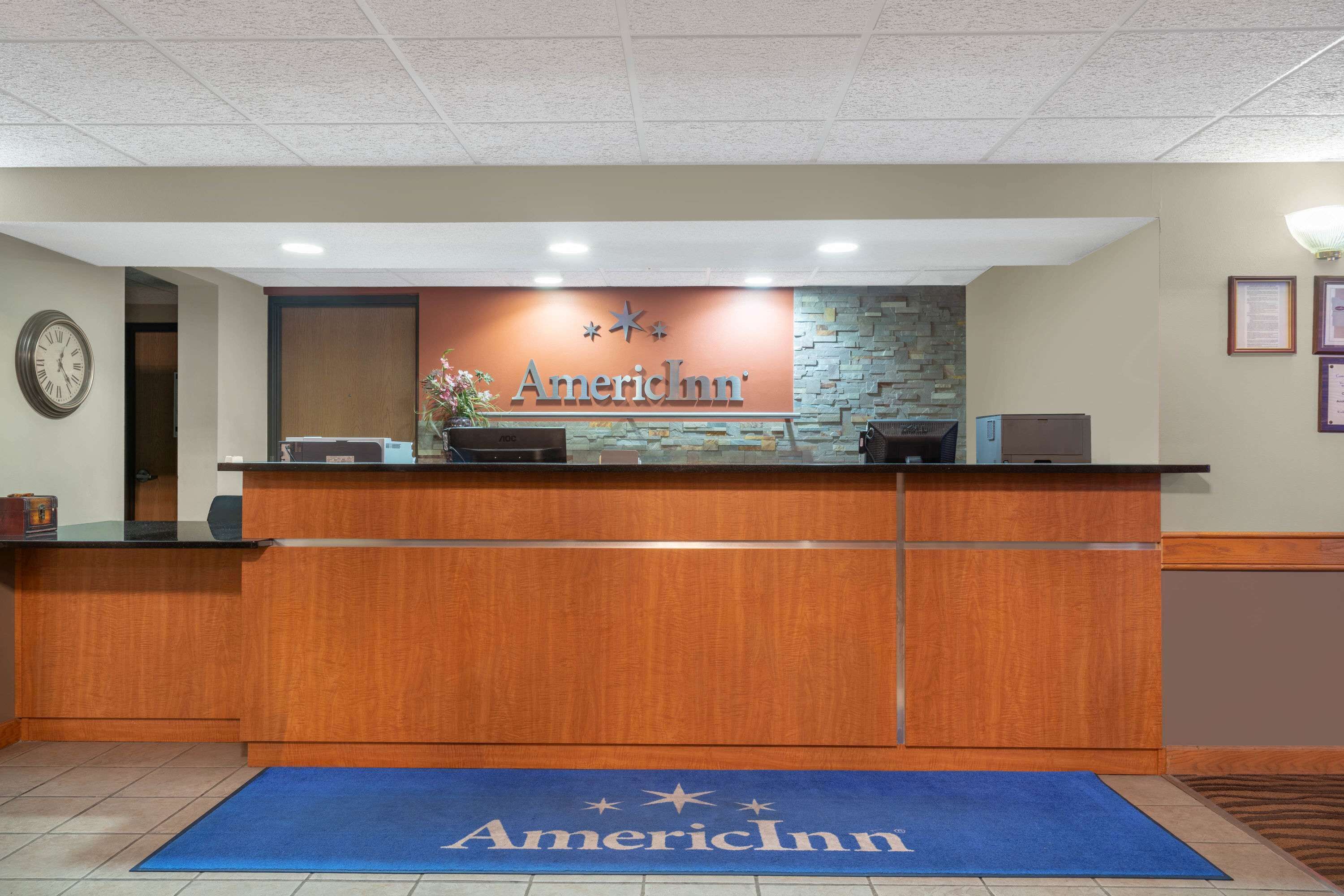 Ein Empfangsschalter mit einer Uhr, einem Schild mit der Aufschrift 'American Inn' und einem blauen Teppich mit dem passenden Logo.