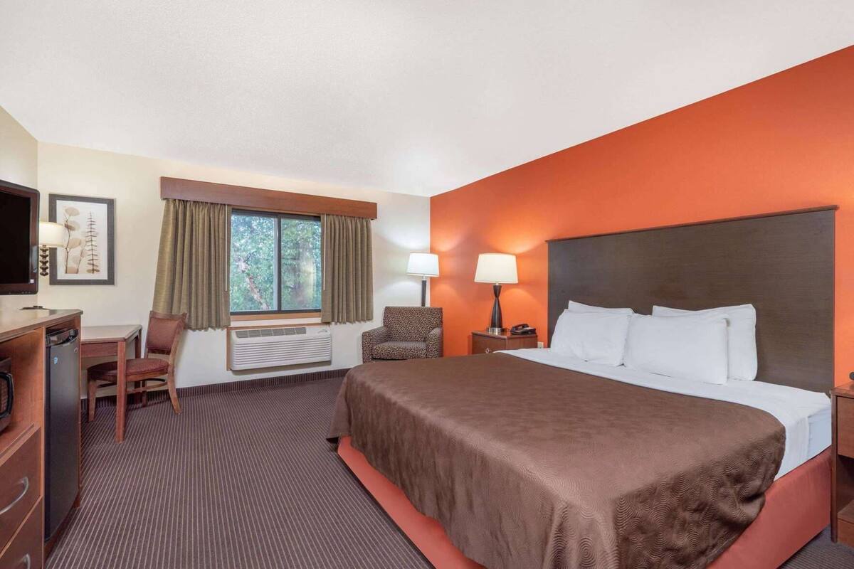 Habitación de hotel con cama, escritorio, silla, televisor y ventana con cortinas.