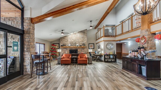 A spacious living area with a stone fireplace, wooden beams, and a Christmas tree. - AmericInn by Wyndham Coon Rapids (Coon Rapids)