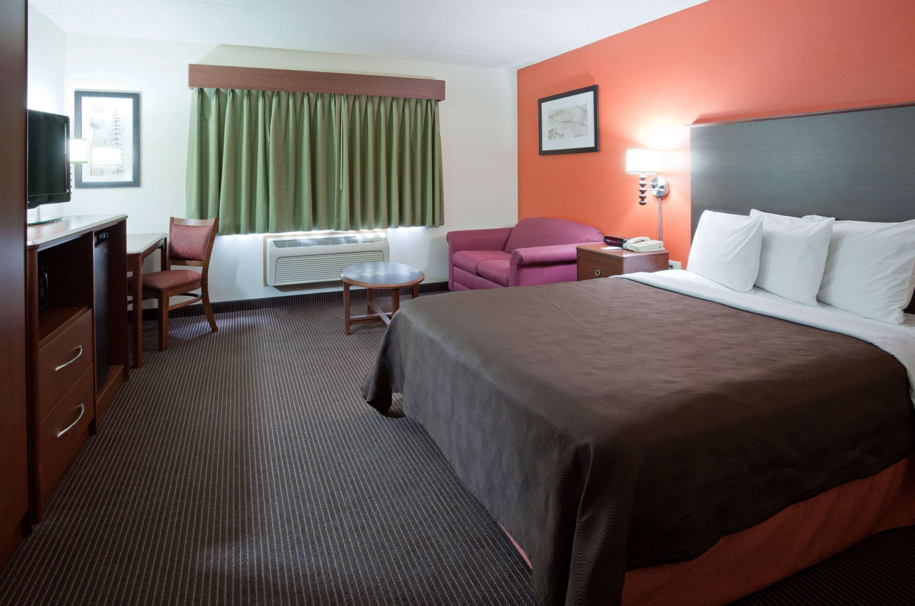 A hotel room with a large bed, a desk with a chair, a small table, and a couch.