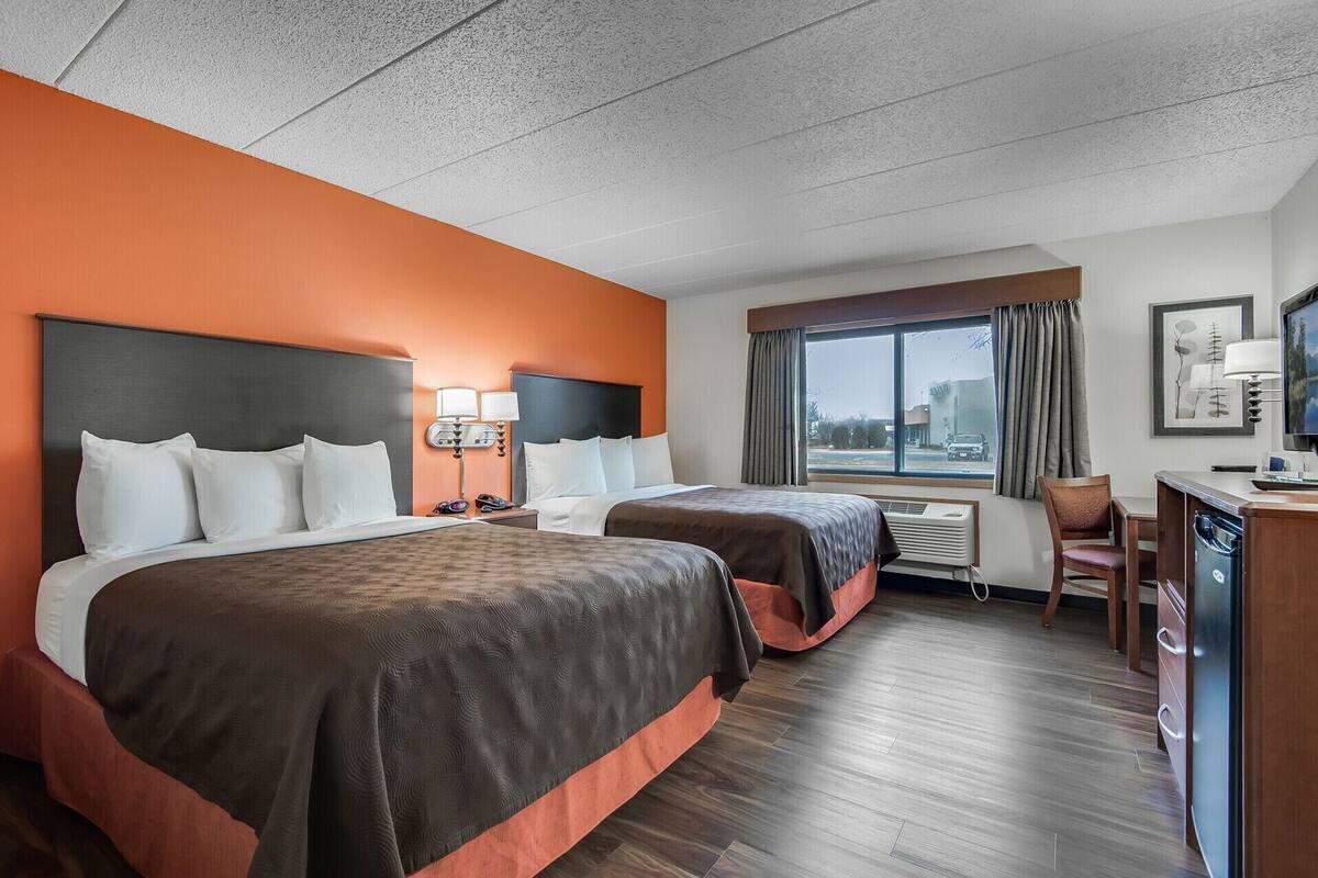 Una habitación de hotel con dos camas, un escritorio, una silla, un televisor y una ventana con cortinas.