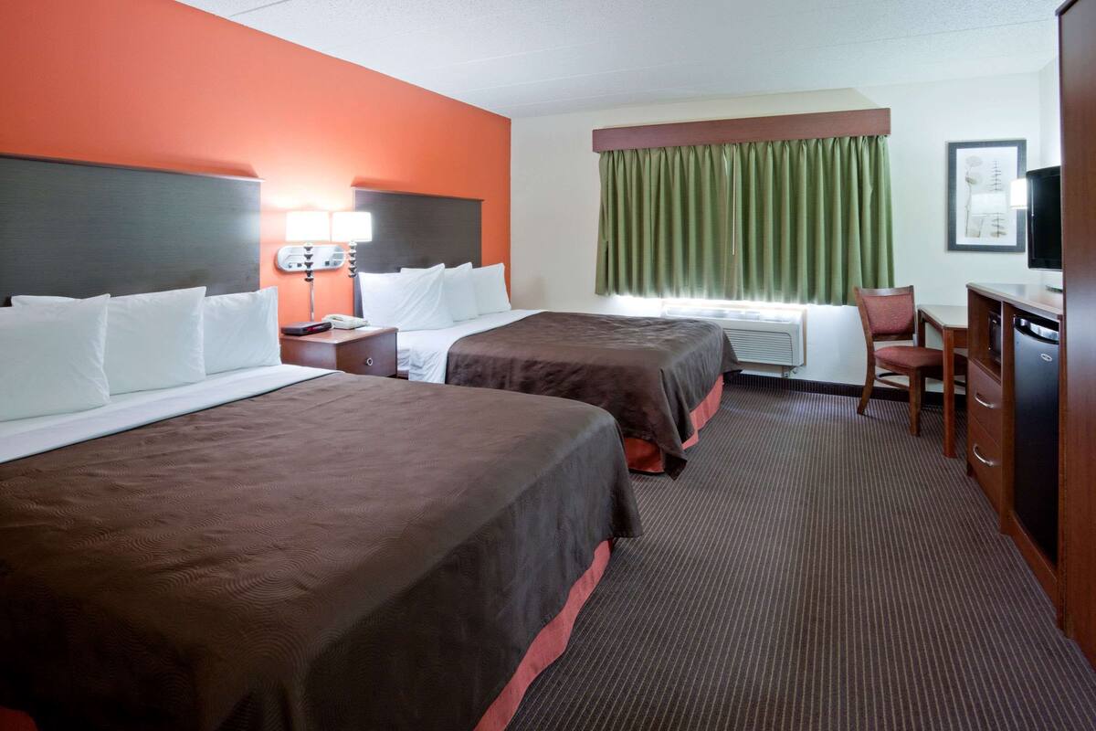 Habitación de hotel con dos camas, un escritorio, una silla, un televisor y una ventana con cortinas.