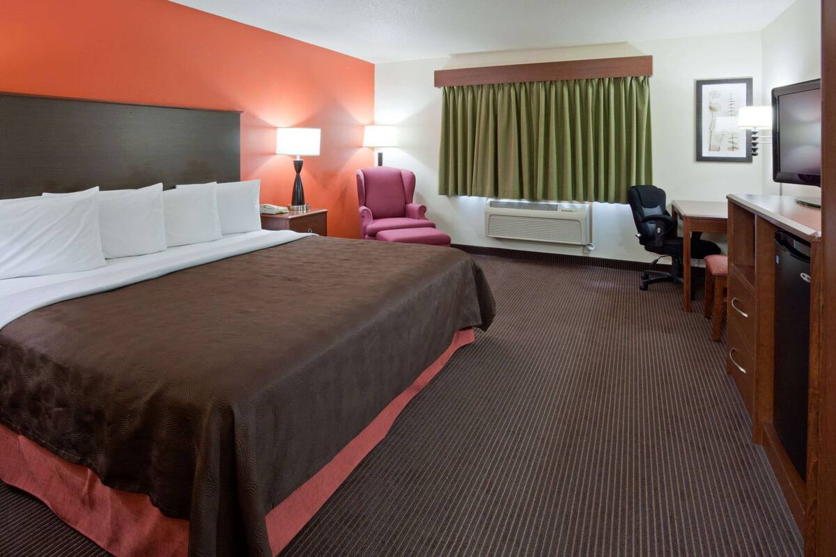 Habitación de hotel con una cama grande, un escritorio, una silla, un televisor y una ventana con cortinas.