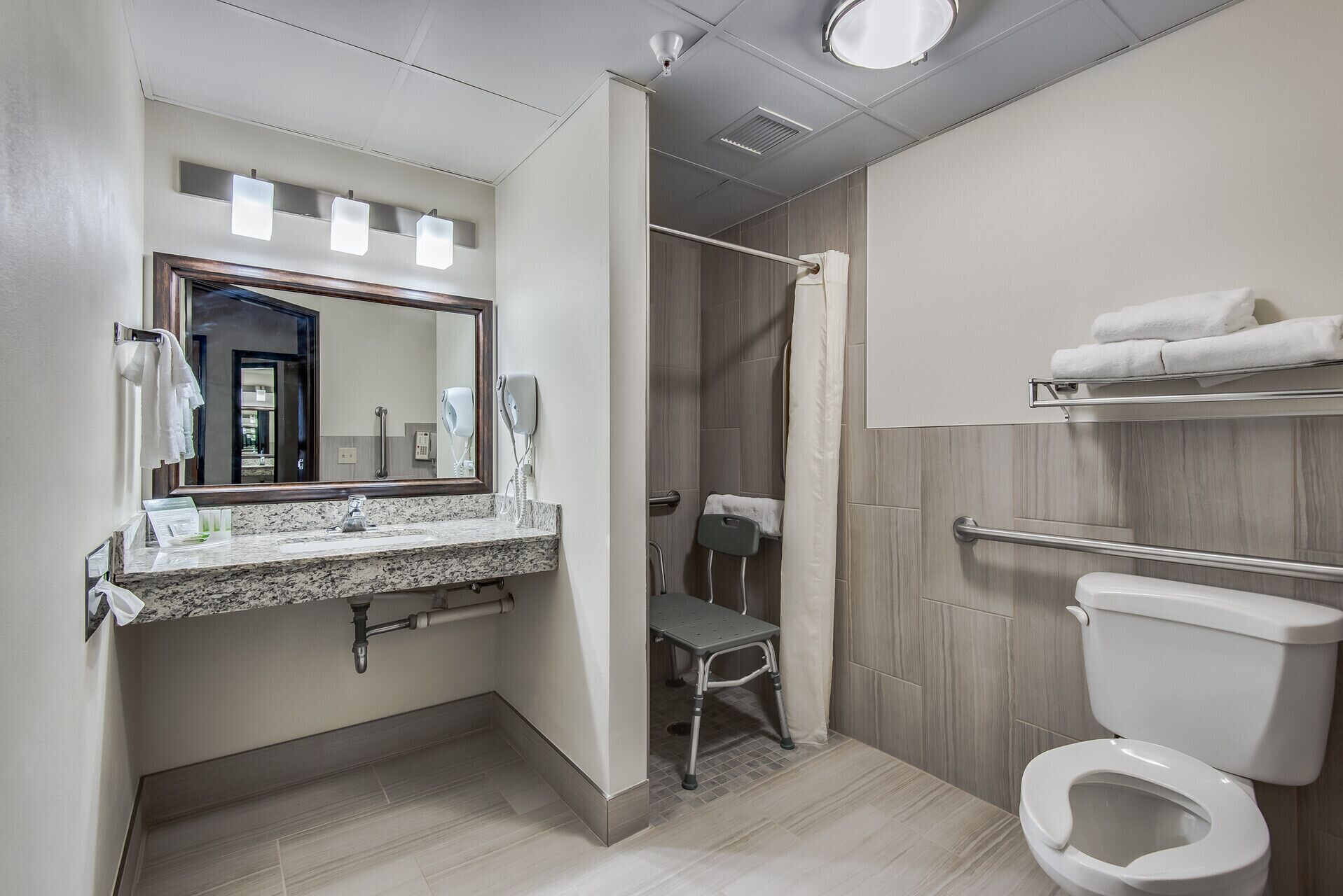 Un baño moderno con encimera de granito, ducha con puerta de vidrio, barra de apoyo y retrete.