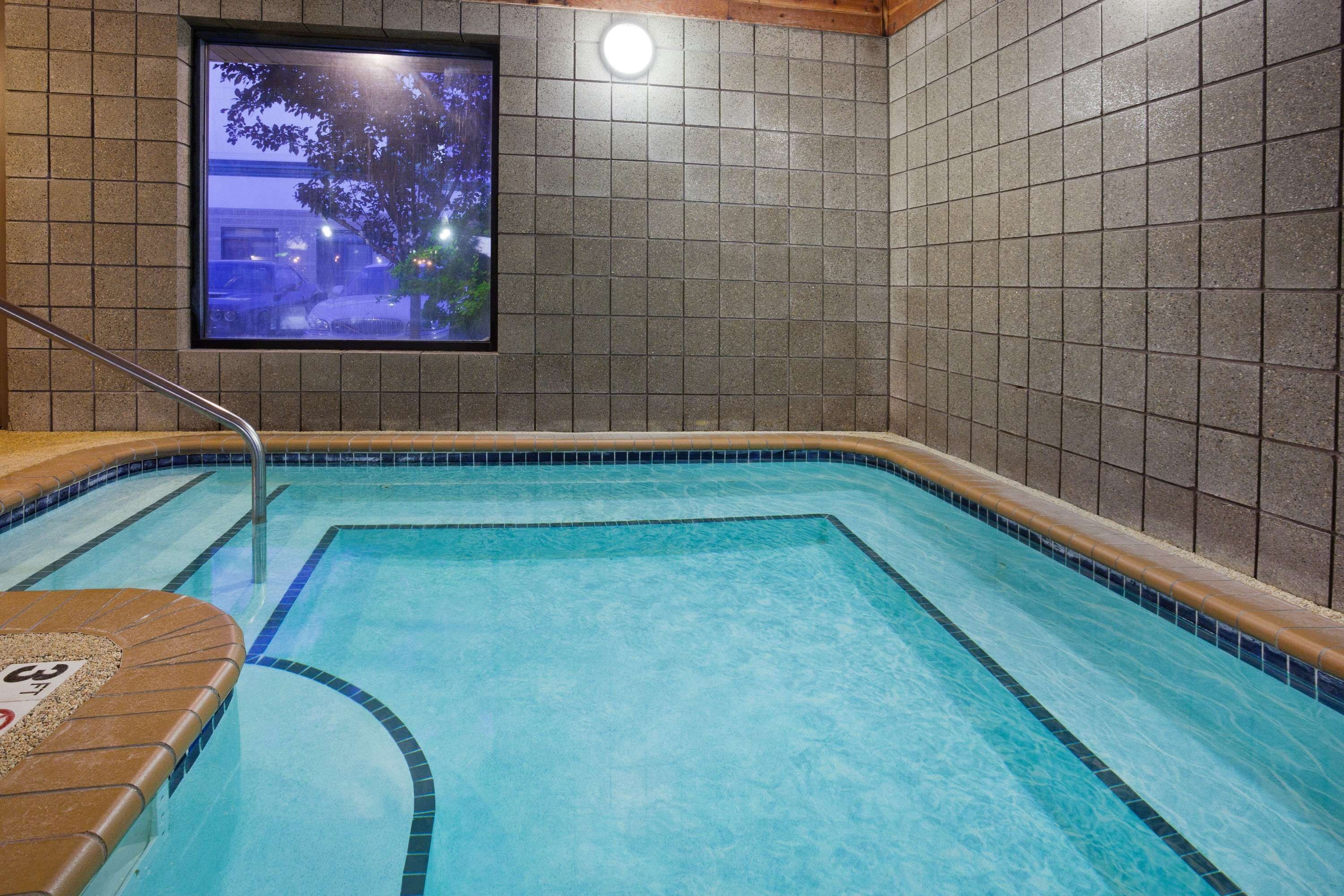 A swimming pool with tiled walls and a window overlooking a parking area.
