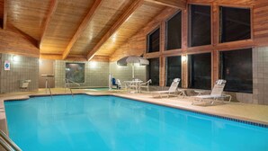 An indoor swimming pool with wooden beams, tiled walls, and lounge chairs. - AmericInn by Wyndham Coon Rapids (Coon Rapids)