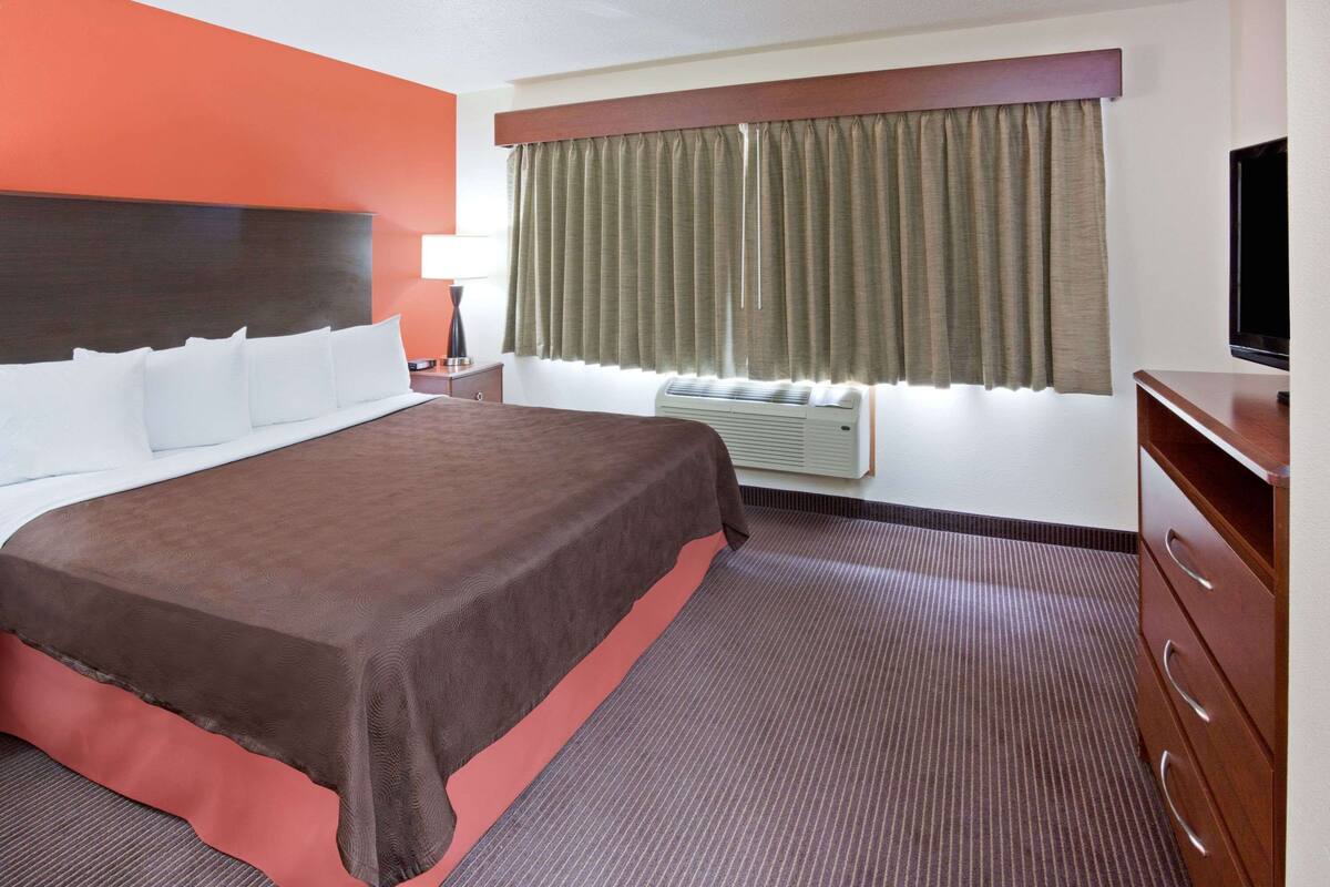 Una habitación de hotel con una cama grande, un televisor de pantalla plana, un aparador y una ventana con cortinas.