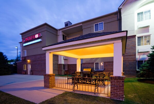 Un hôtel doté d’un espace extérieur couvert avec des sièges, d’une façade en briques et d’une enseigne indiquant qu’il s’agit d’un établissement Candlewood Suites.