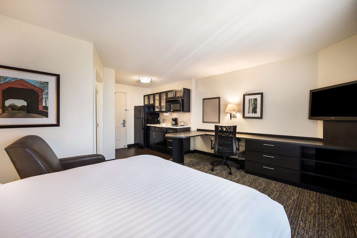 Habitación de hotel con una cama grande, un escritorio, una silla, un televisor, un microondas y un refrigerador.