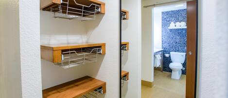 A bathroom with a toilet, a sink, and a mirror. There are wooden shelves above the sink.