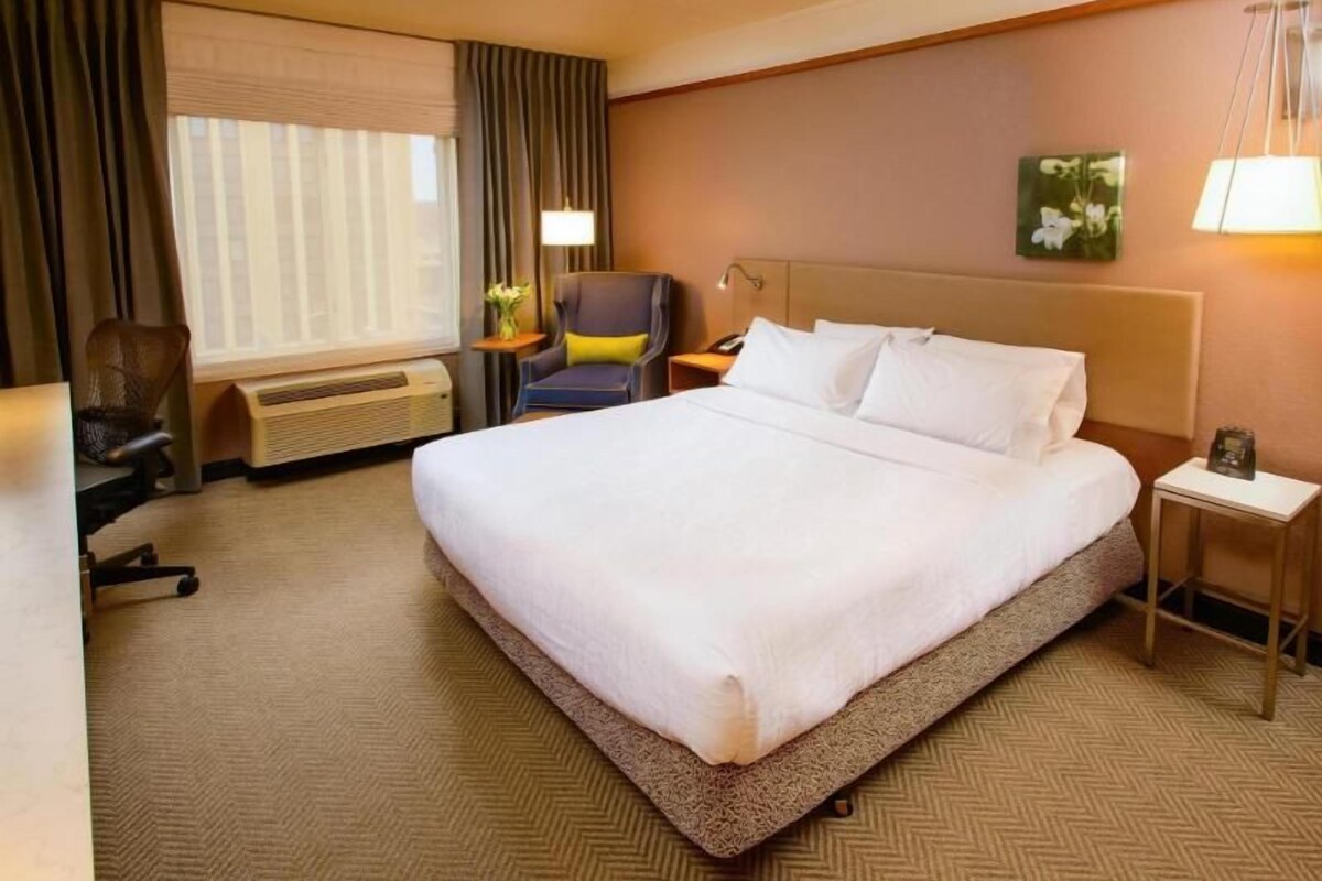 Una habitación de hotel con una cama grande, un escritorio, una silla, una lámpara y una mesita de noche.
