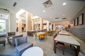 A spacious hotel lobby with multiple seating areas, including sofas and round tables, and a large dining area with yellow chairs. - Hilton Garden Inn Rochester Downtown, MN (Rochester)