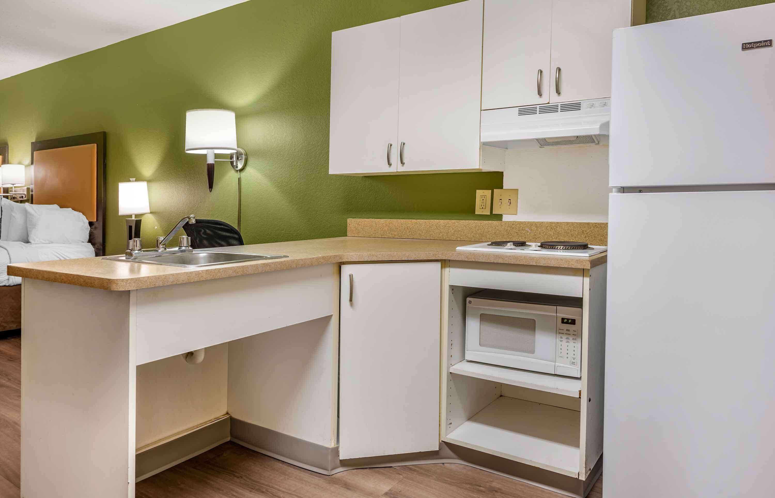 Une cuisine d’hôtel de taille réduite, équipée d’un four à micro-ondes, d’une cuisinière et de meubles blancs.