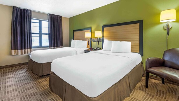 A hotel room with two beds, a window with curtains, a lamp, and a chair.
