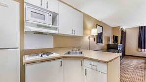 A compact hotel kitchen with a microwave, stove, sink, and white cabinets.