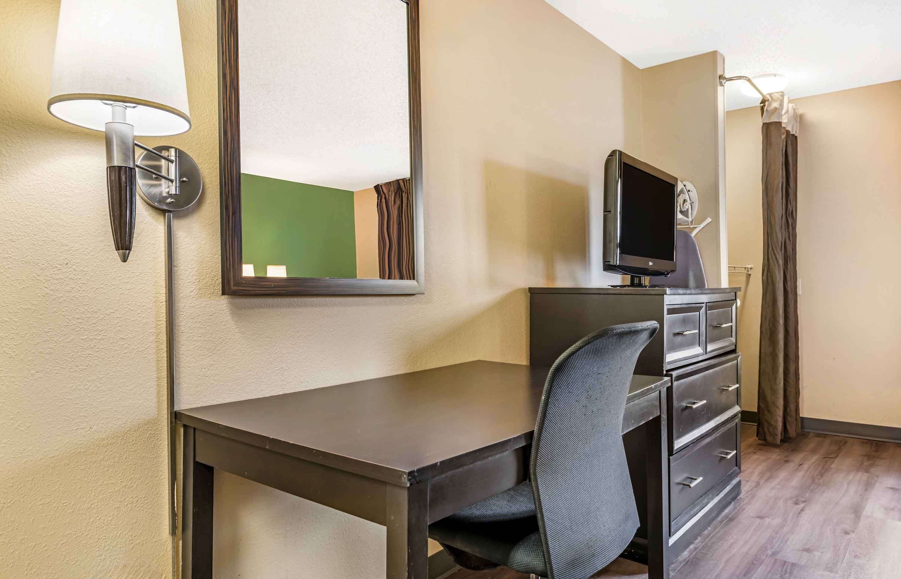 A hotel room with a desk, chair, TV, and a mirror.