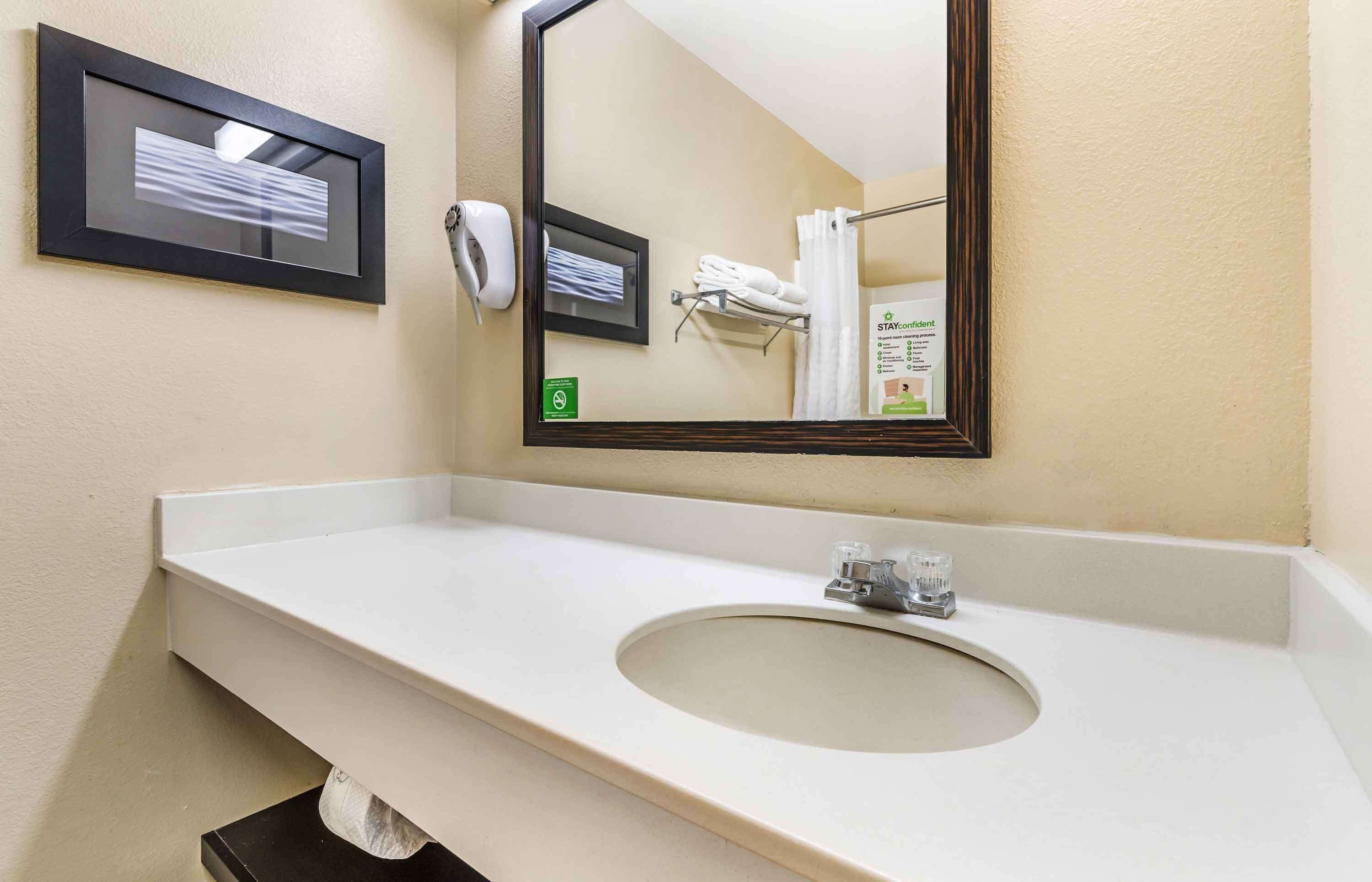A bathroom with a white sink, a mirror, a framed picture, a towel rack, and a hand dryer.
