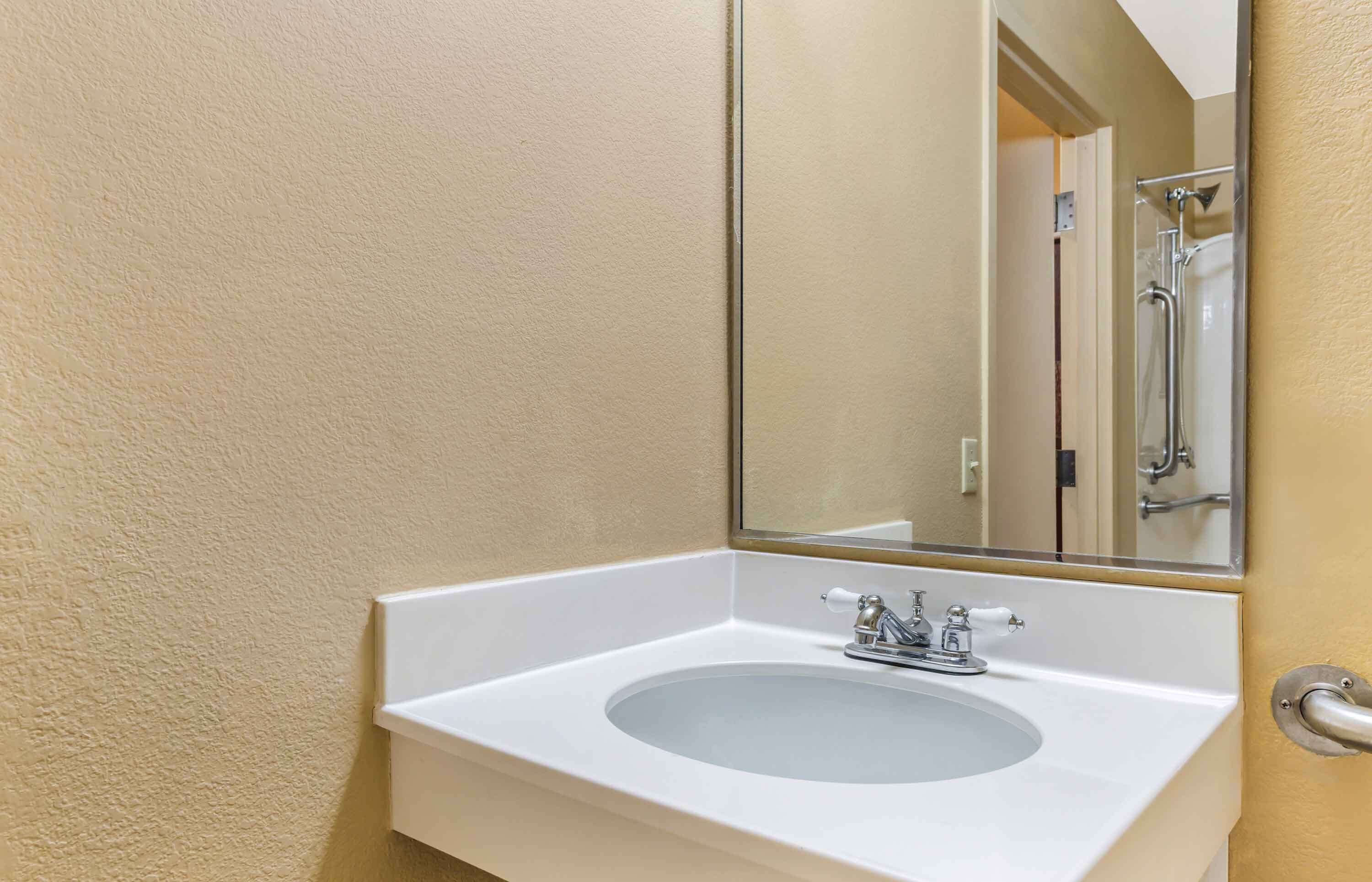 A bathroom with a white sink, a mirror, and a shower visible in the background.