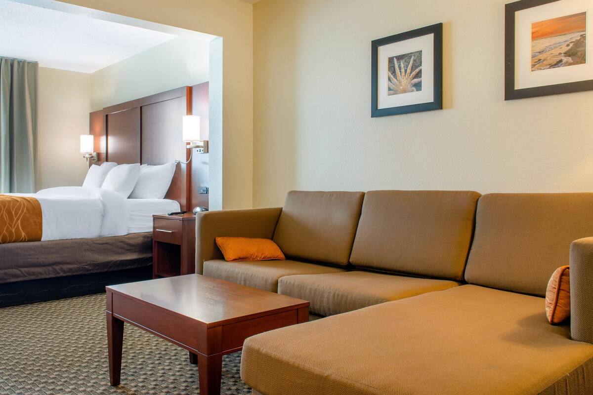 A hotel room with a bed, a sofa, a coffee table, and two framed pictures on the wall.