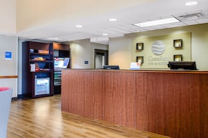 A reception desk with a sign for Comfort Inn & Suites, a vending machine, and a small refrigerator.