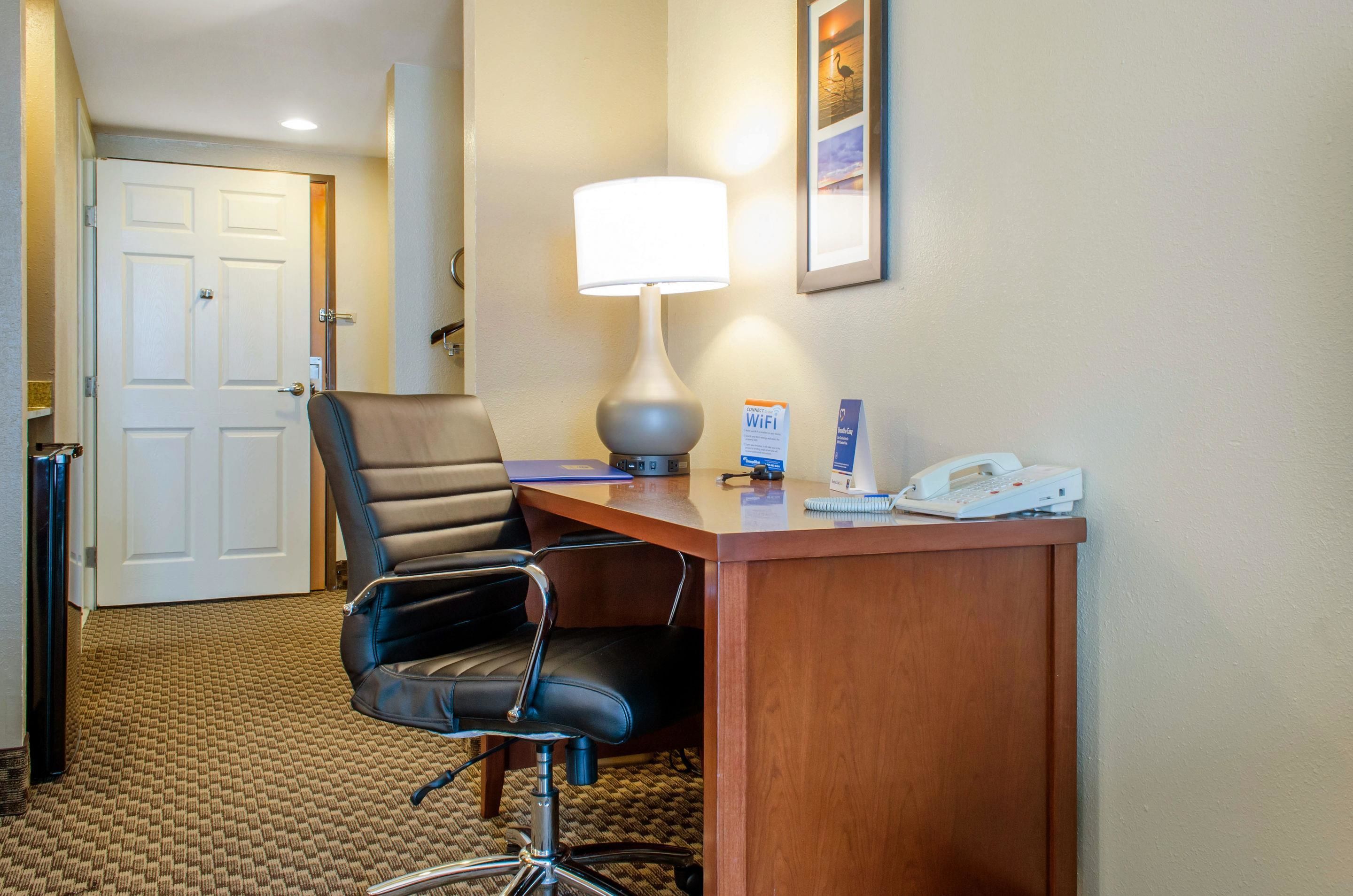 Ein Hotelzimmer mit Schreibtisch, Stuhl, Lampe, Telefon und Tür.