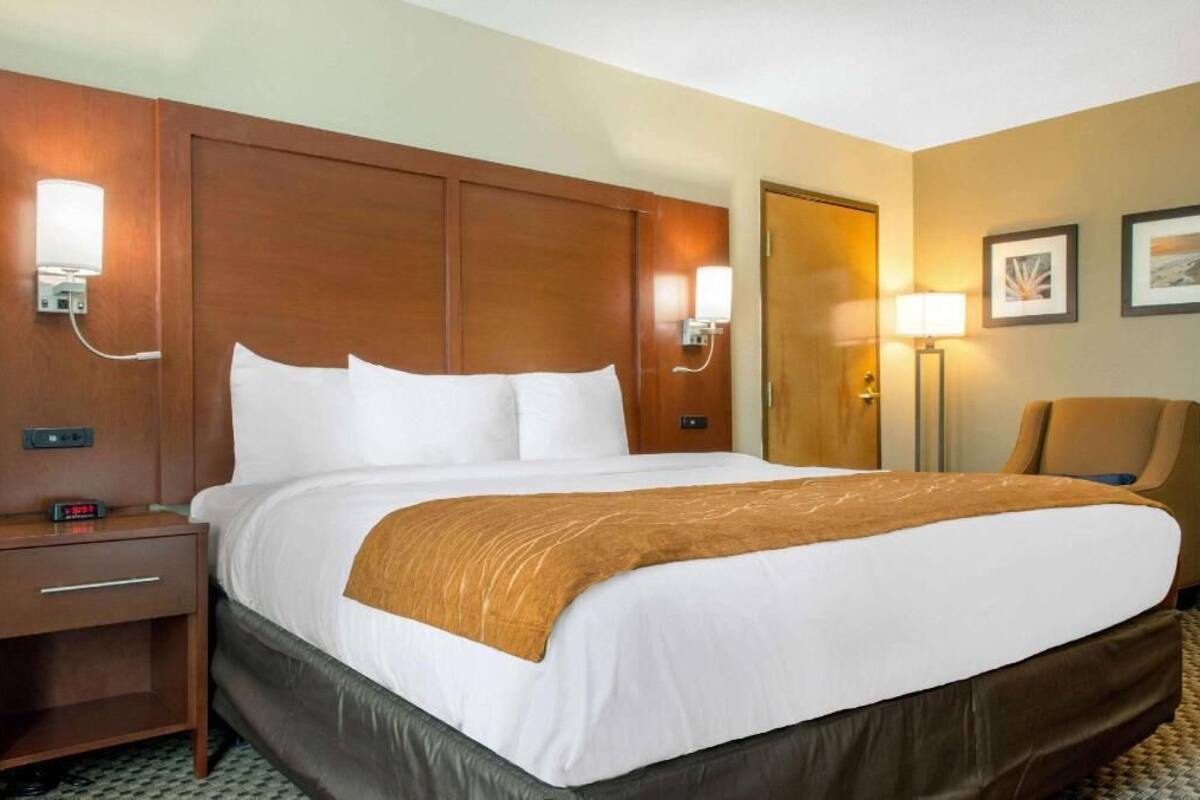 A hotel room with a large bed, a nightstand, a desk, a chair, and a door.