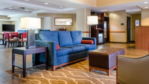 Eine Hotellobby mit einem blauen Sofa, einem braunen Hocker, einem kleinen Tisch und einem Fernseher im Hintergrund.