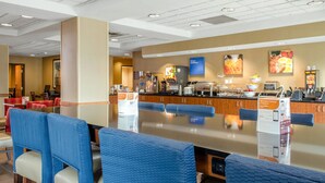 Ein Frühstücksbereich eines Hotels mit einer langen Theke, blauen gepolsterten Stühlen und verschiedenen Speisen- und Getränkeauslagen.