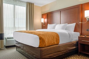 Habitación de hotel con una cama grande, una mesita de noche, una lámpara de pared y una ventana con cortinas.