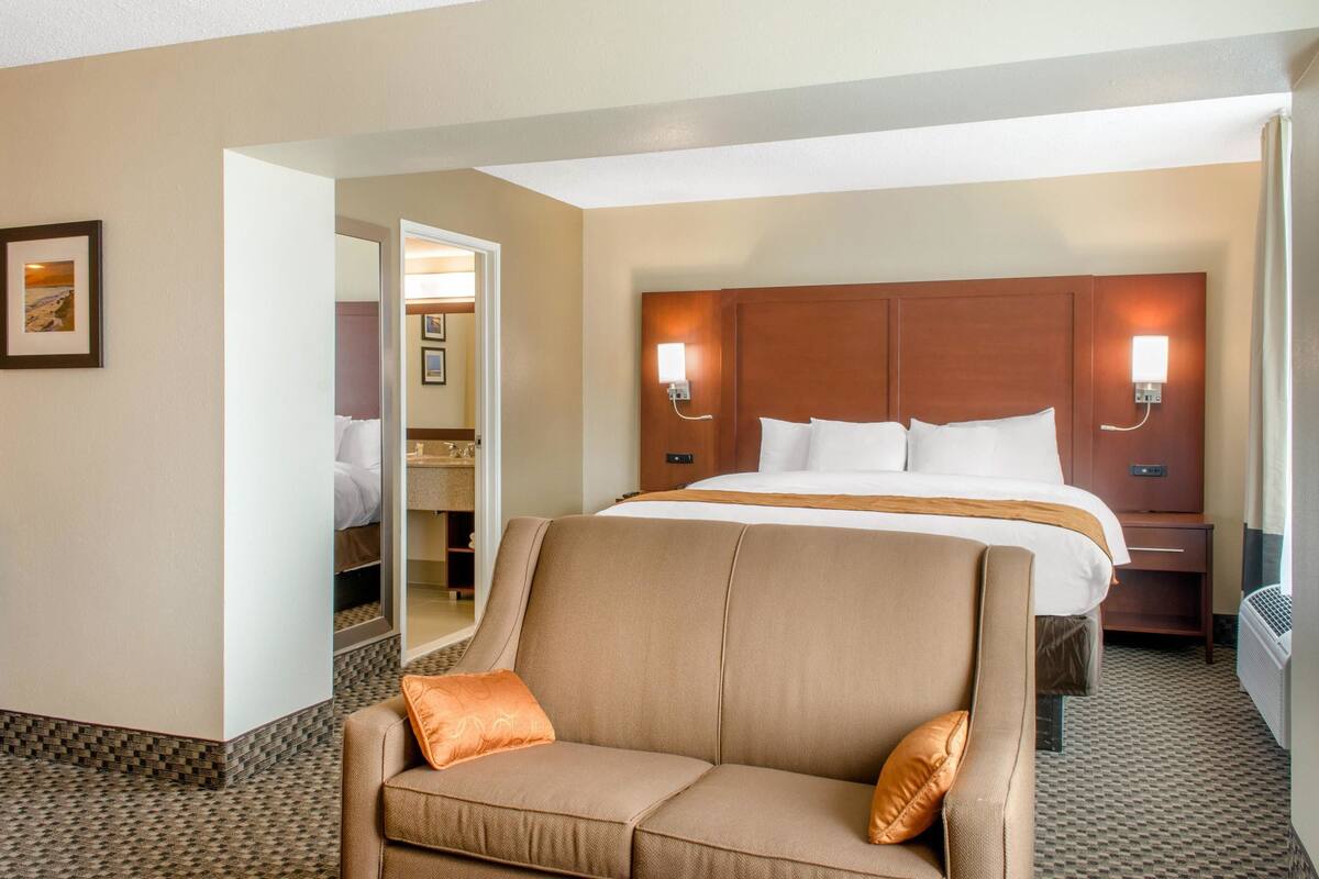 A hotel room with a large bed, a sofa, a mirror, and two wall-mounted lights.