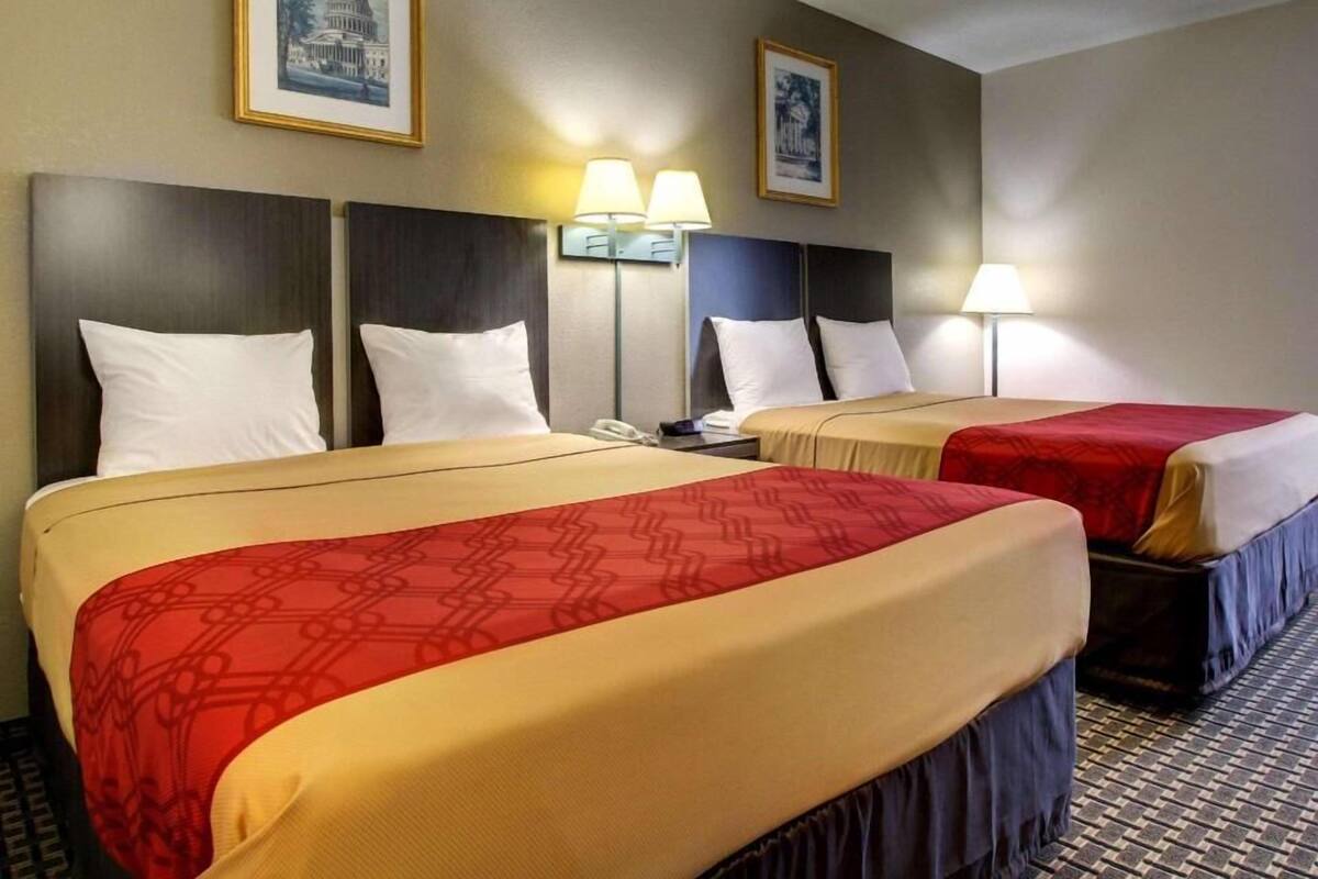 A hotel room with two beds, each with a headboard, bedside lamps, and a telephone.