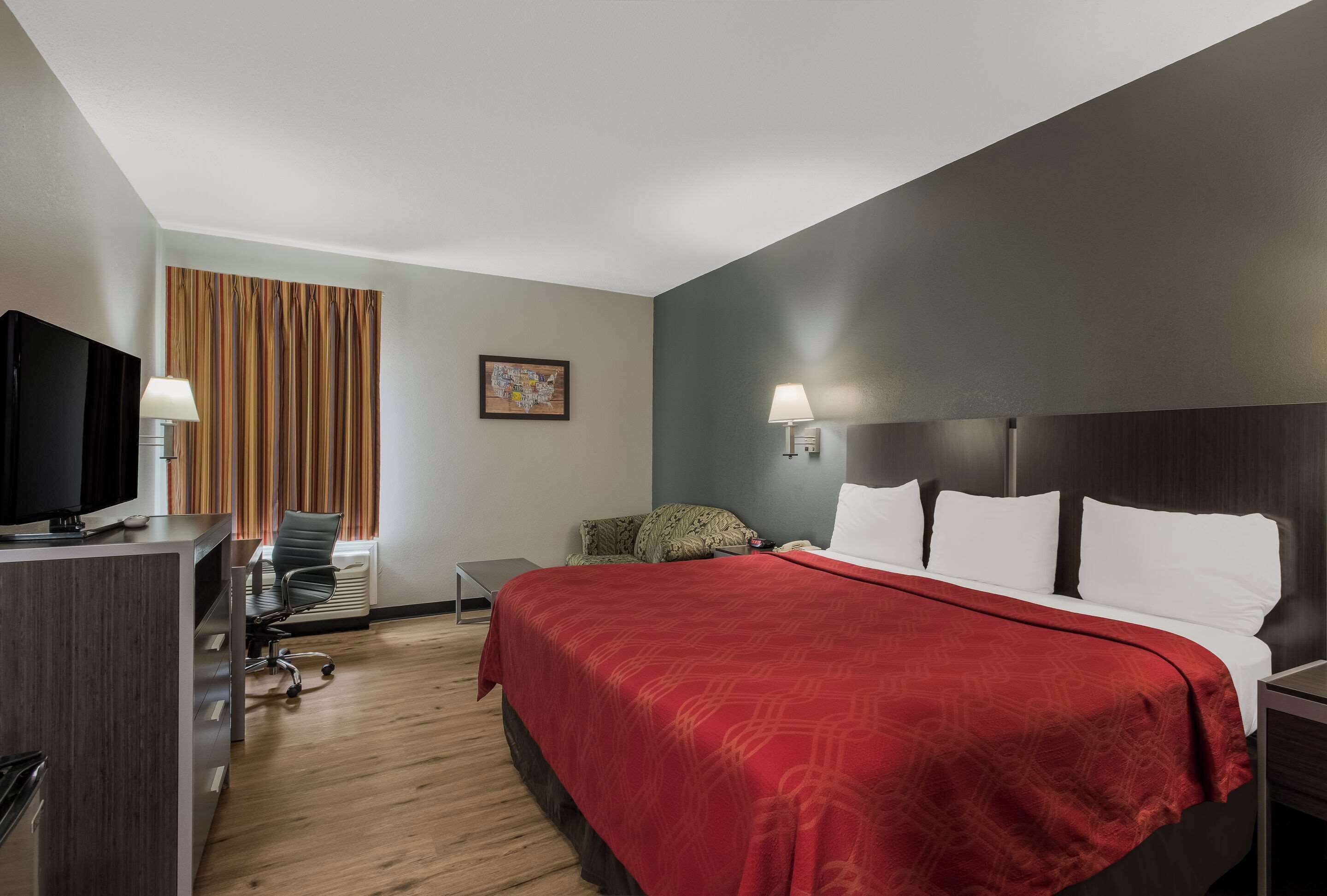 A hotel room with a large bed, a desk with a television, a chair, and a window with curtains.
