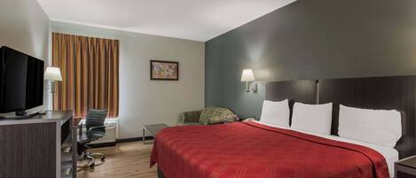 A hotel room with a large bed, a desk with a television, a chair, and a window with curtains.