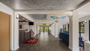 A hotel lobby with a wooden floor, a reception desk, a blue sofa, and a chandelier.