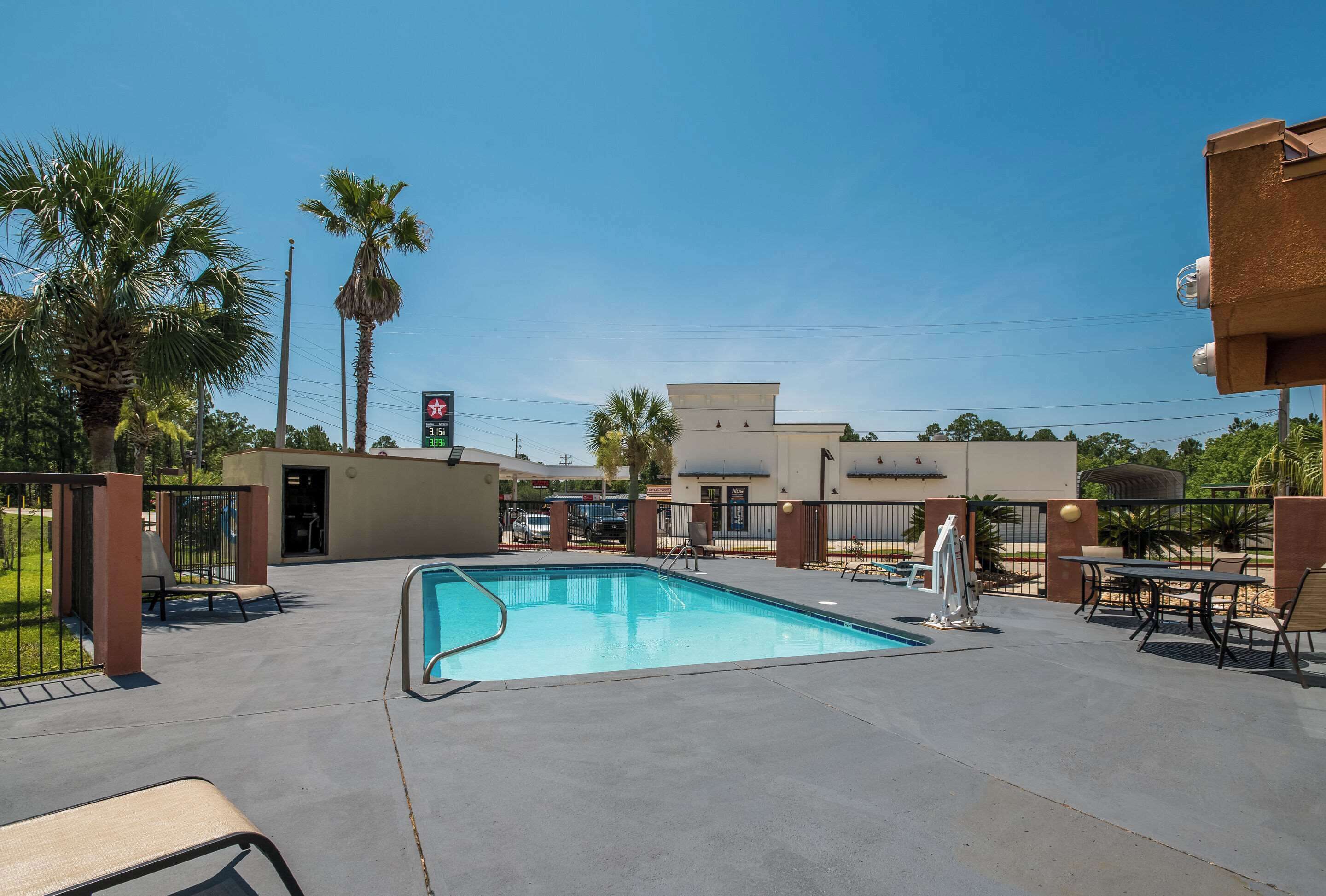 A swimming pool with lounge chairs and tables, surrounded by palm trees and a building with a sign.