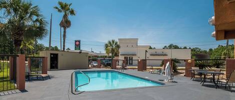 A swimming pool with lounge chairs and tables, surrounded by palm trees and a building with a sign.