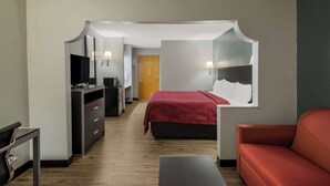 A hotel room with a bed, a desk, a TV, and a red sofa.
