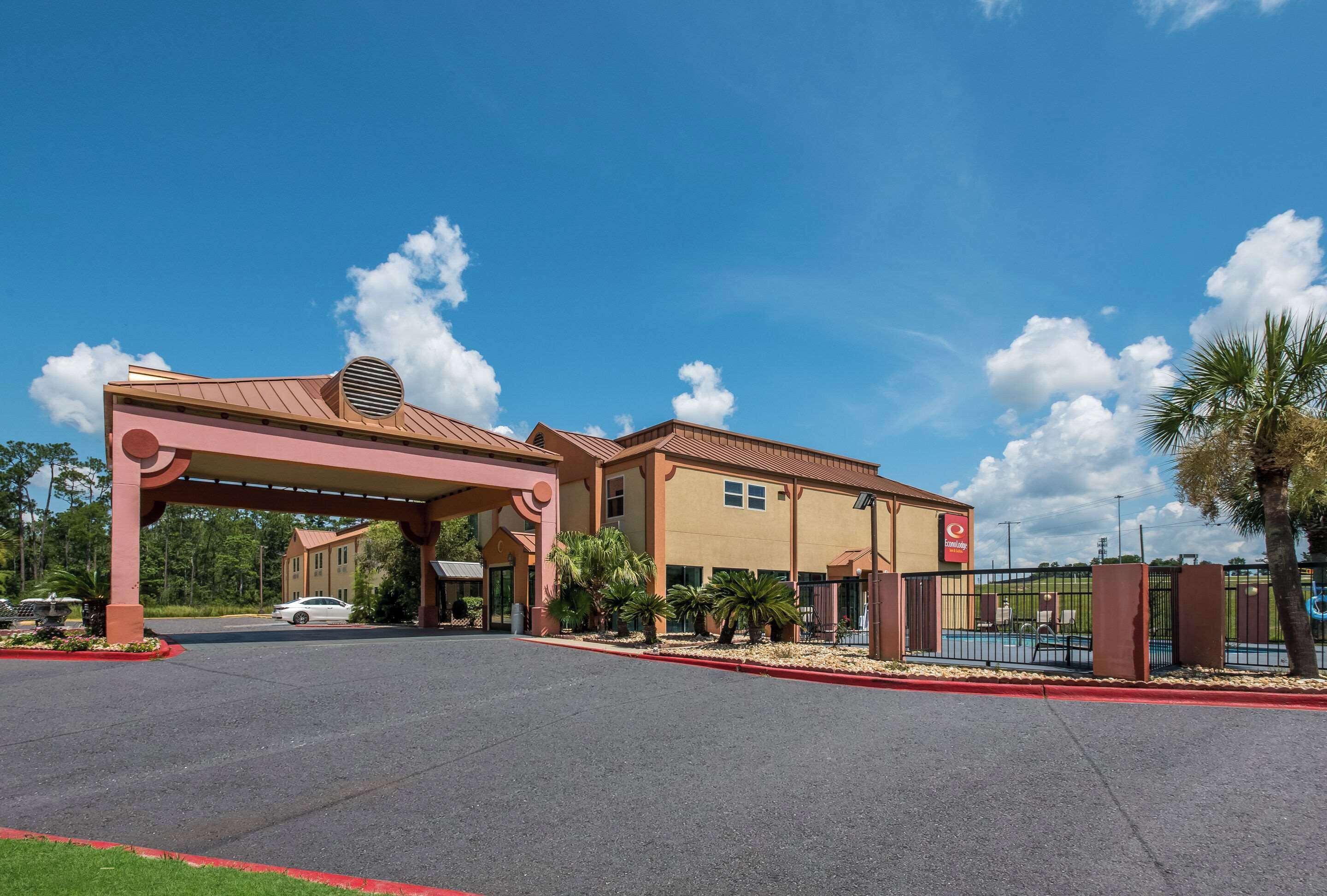 A hotel entrance with a covered walkway, palm trees, and a clear blue sky.