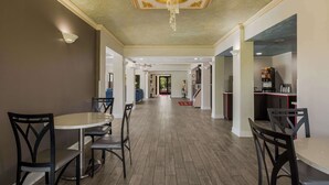 A spacious hallway with a chandelier, a round table with chairs, and a kitchen area with red accents.