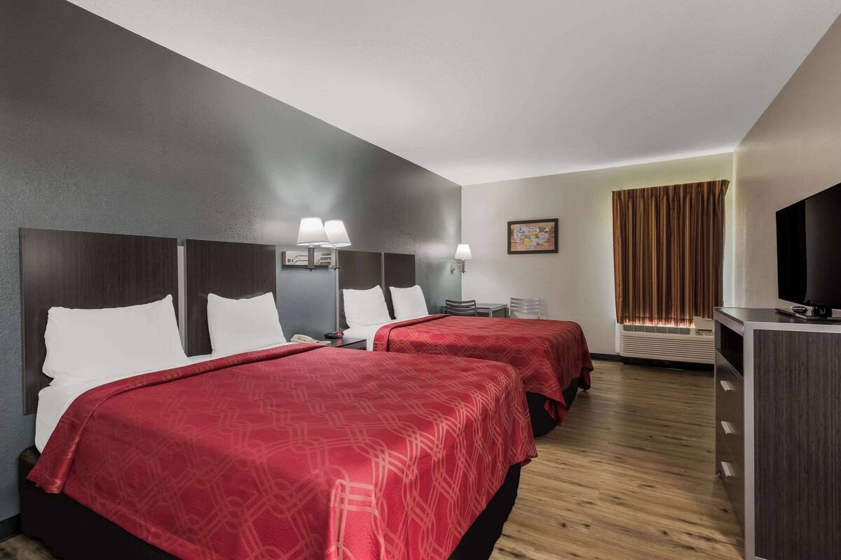 A hotel room with two beds, a desk, a TV, and a window with curtains.