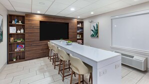 A modern kitchen with a central island, bar stools, built-in shelves, a large flat-screen TV, and a whiteboard. - Wingate by Wyndham Hattiesburg (Hattiesburg)
