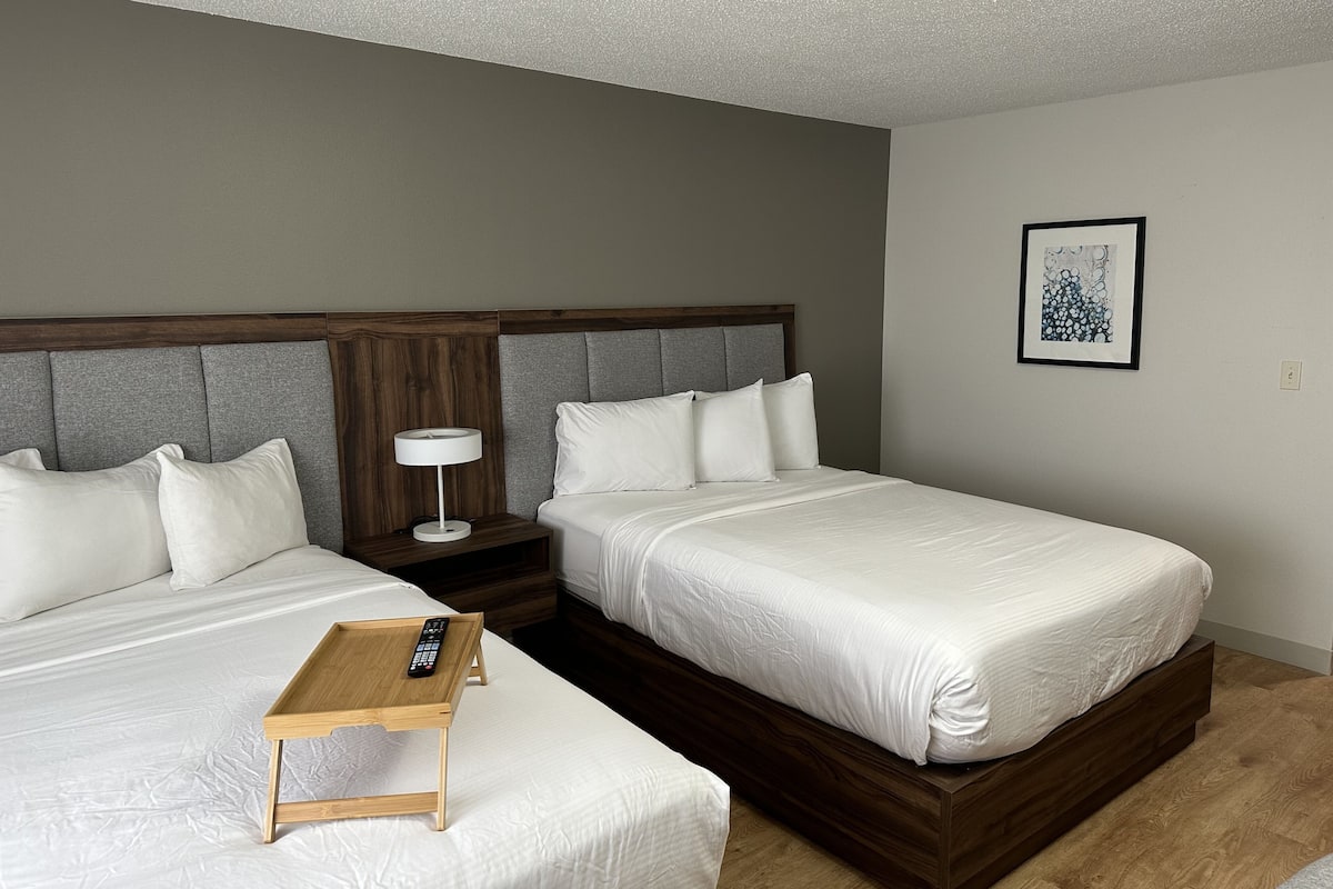 Habitación de hotel con dos camas, una mesita de noche, una lámpara y un cuadro en la pared.