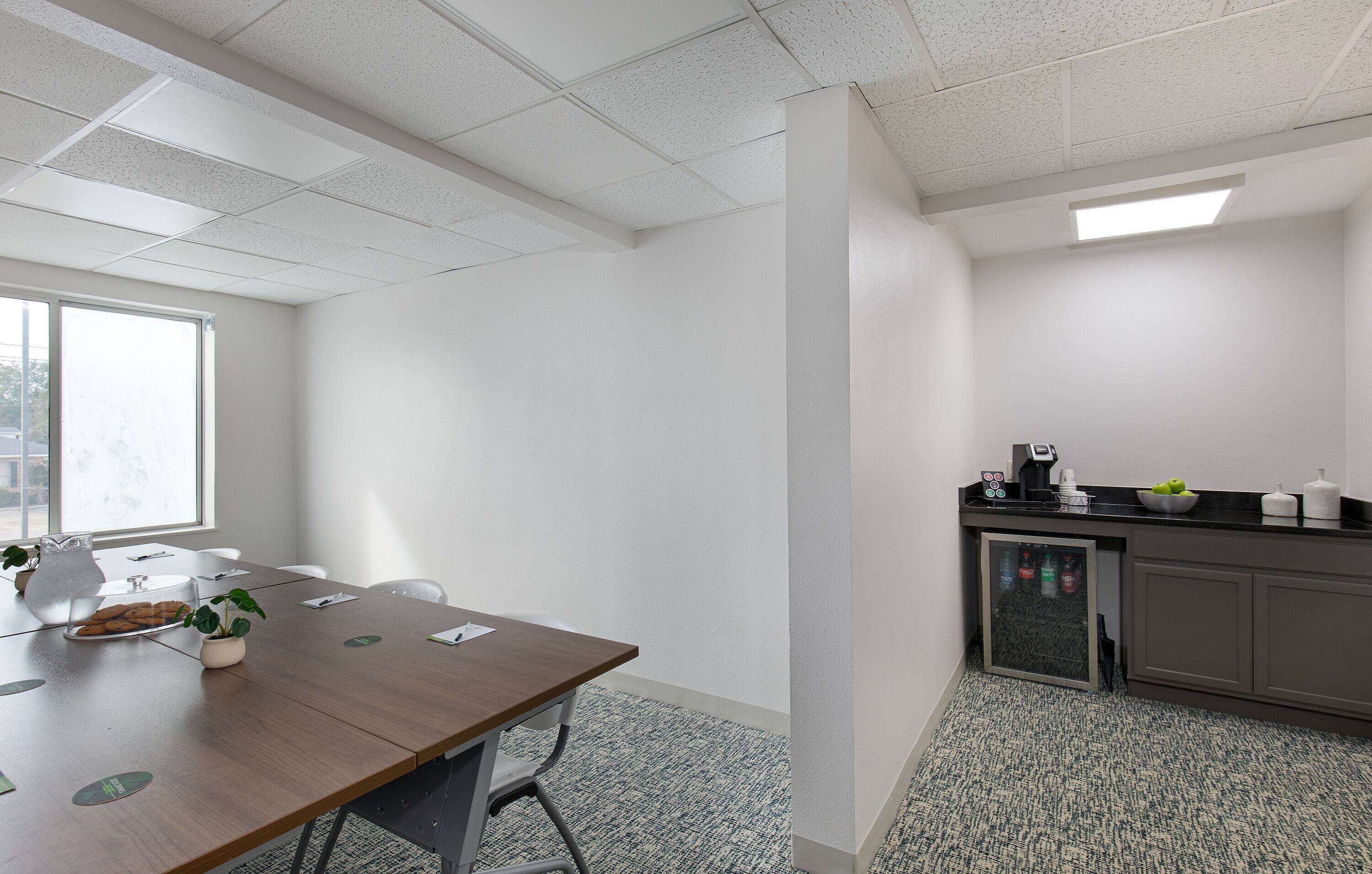 A conference room with a wooden table, chairs, a small plant, and a window.