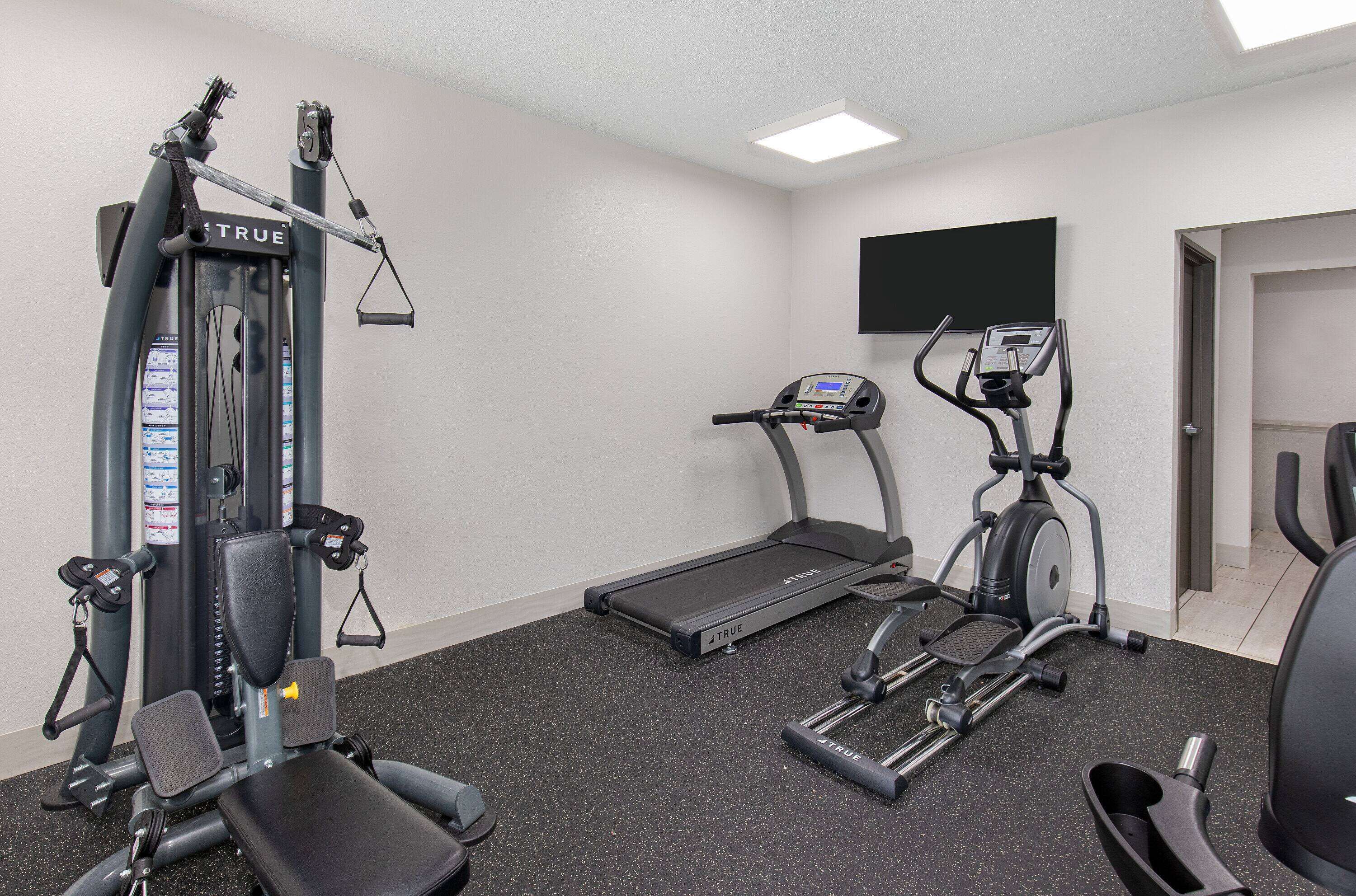 A gym with a treadmill, elliptical, and weight machine.