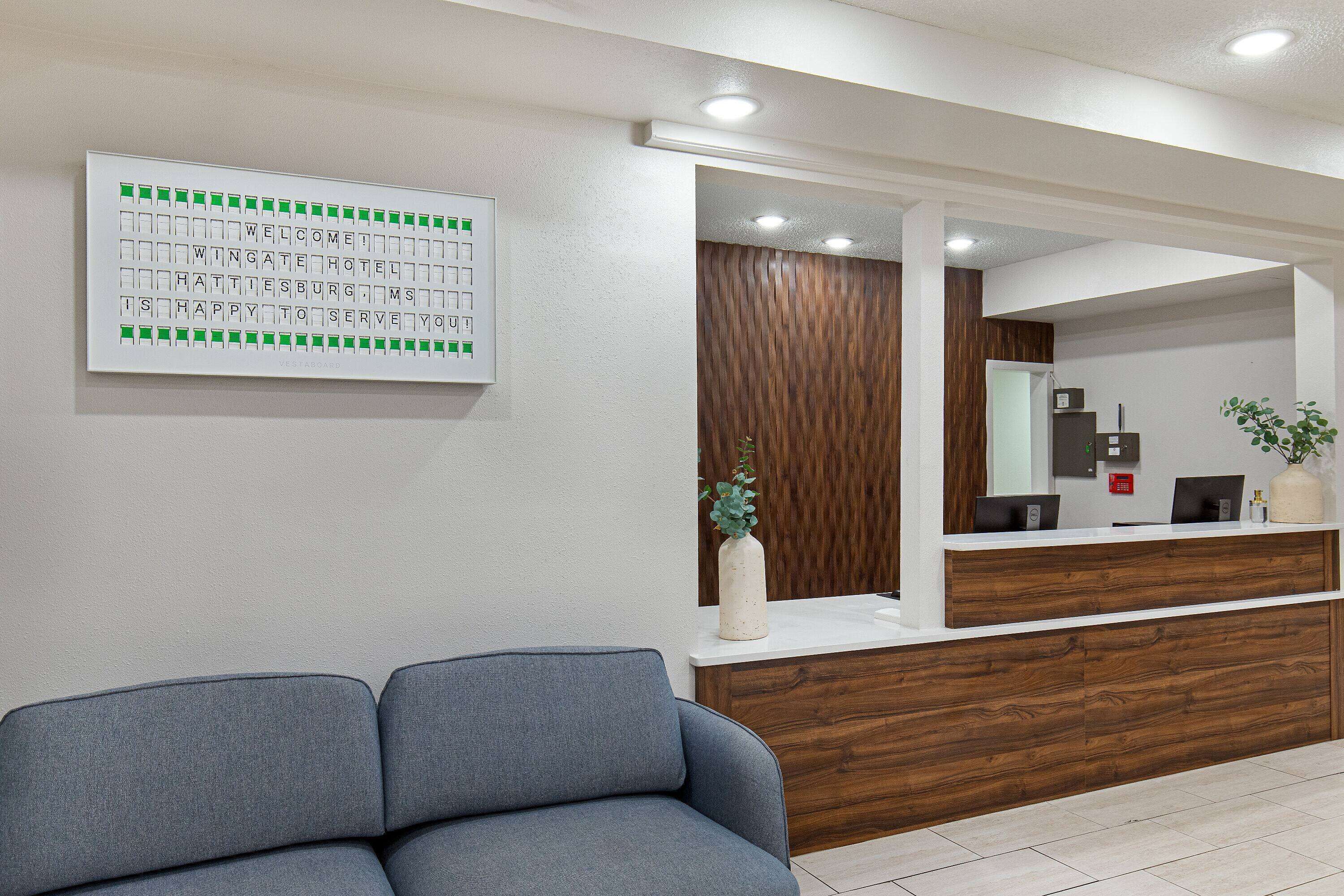 Zona de recepción con mostrador de madera, área de descanso con sofá y un panel informativo en la pared.