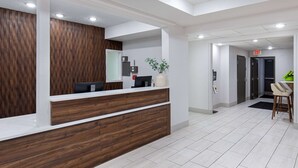 A reception area with a wooden reception desk, a plant, and a seating area with a chair and a small table. - Wingate by Wyndham Hattiesburg (Hattiesburg)