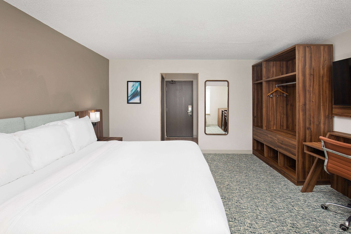 Habitación de hotel con una cama grande, un armario de madera, un espejo y un televisor.