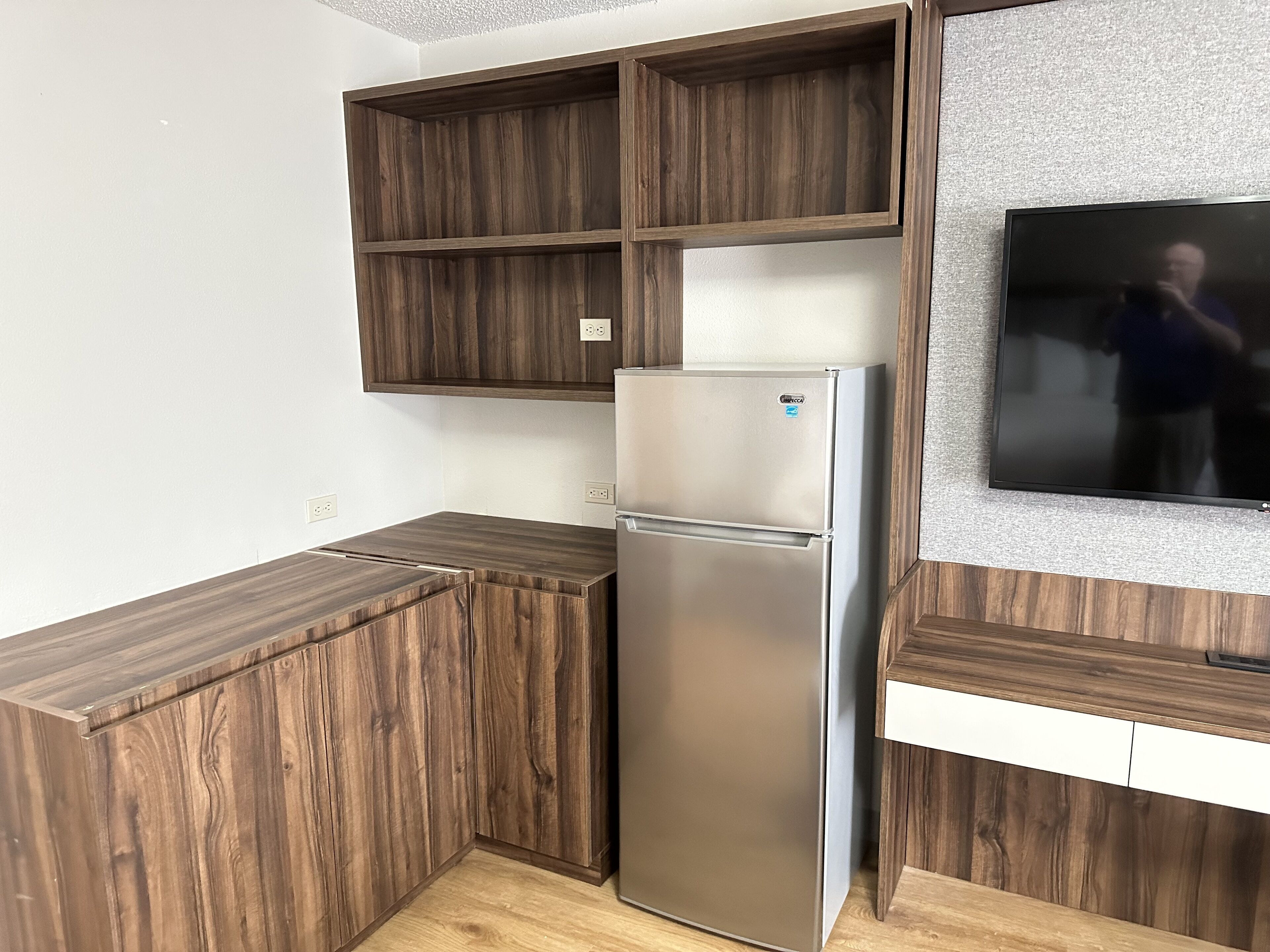 Una cocina con refrigerador empotrado, armarios de madera y televisor montado en la pared.