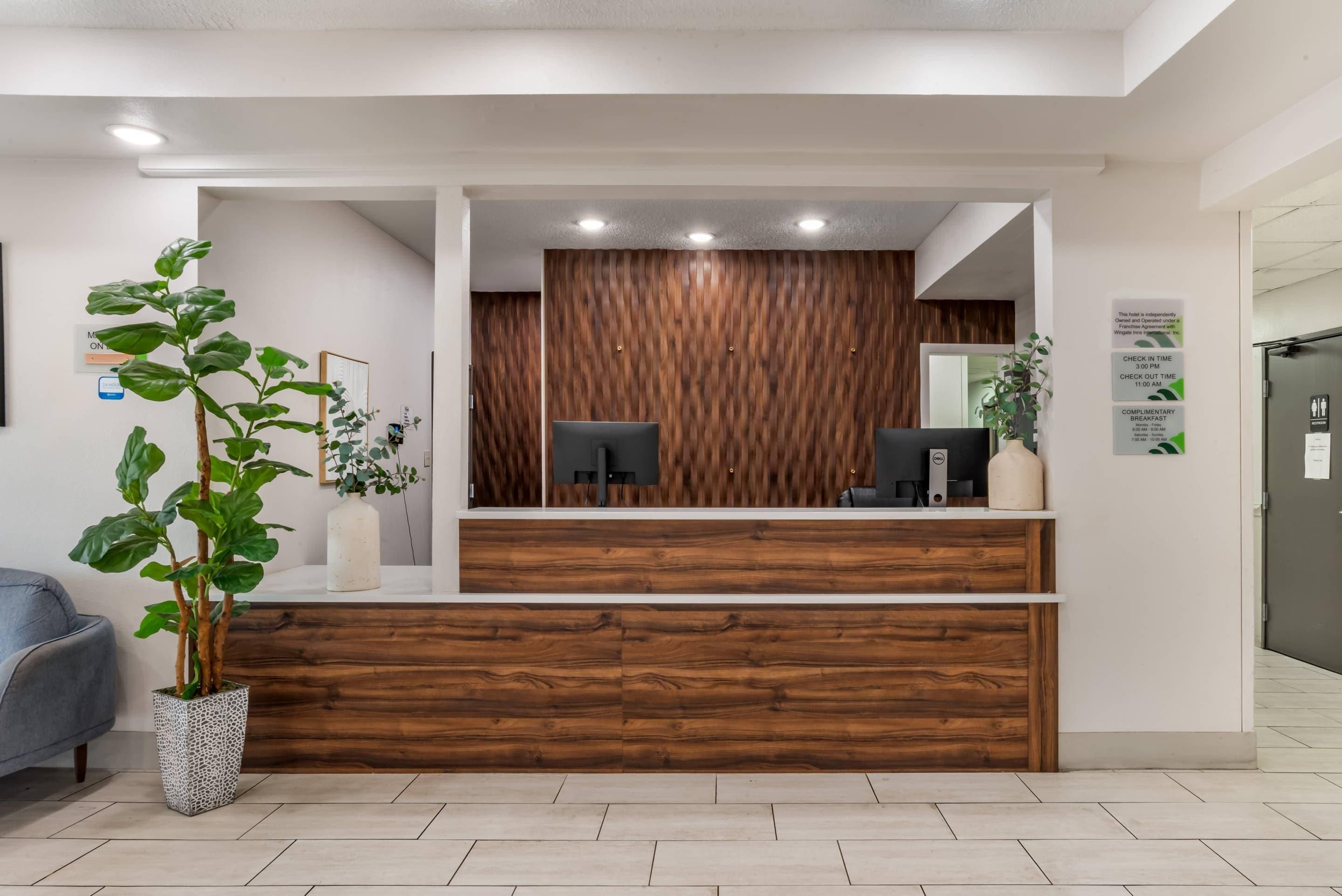 A reception desk with a wooden panel backdrop, a computer, and a plant.